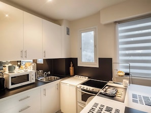 A compact kitchen with white cabinets, a microwave, a stove, and a sink. - SURCOUF (Cannes)