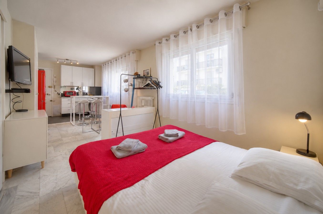 A hotel room with a bed, a desk, a chair, a small kitchenette, and a bathroom.