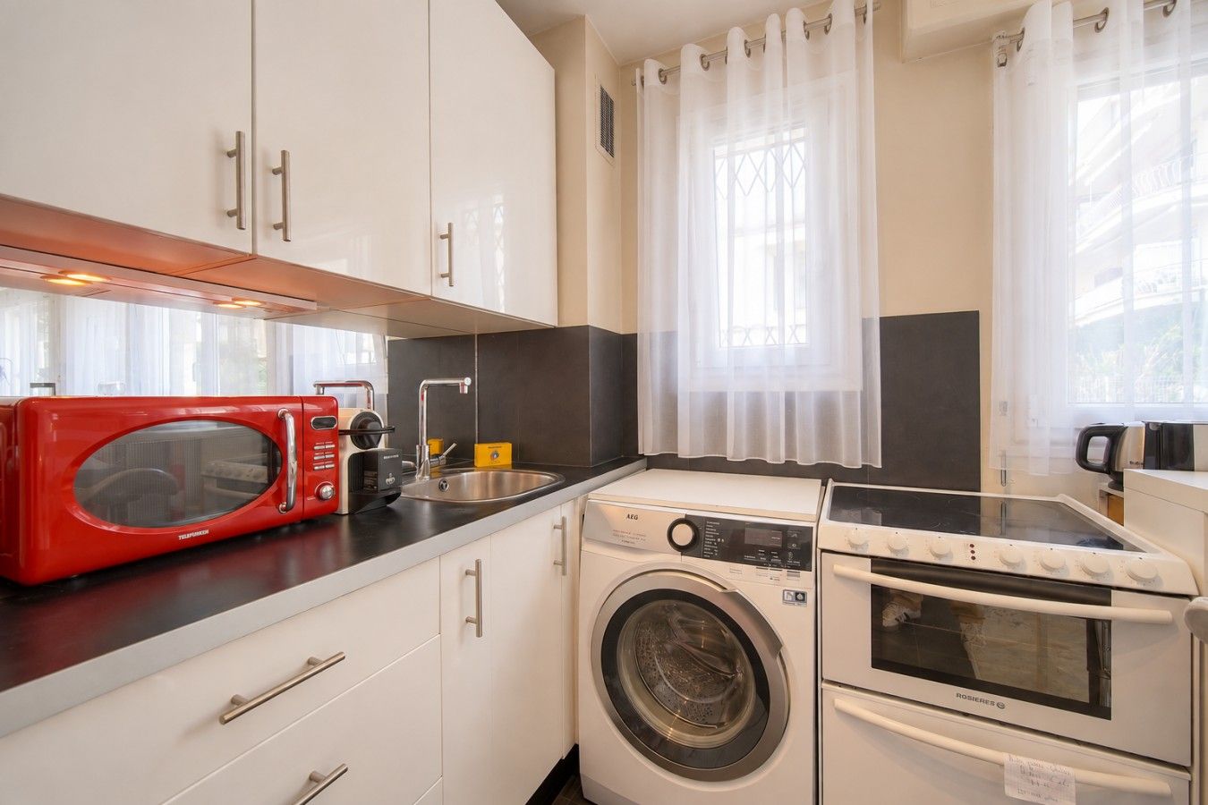 A compact kitchen with a red microwave, a washing machine, and a stove.