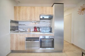 Eine kleine Küche mit Holzschränken, einem Einbauofen und einem Edelstahlkühlschrank.