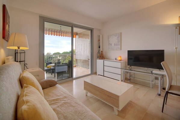A modern living room with a sofa, coffee table, TV, and a balcony with a view. - 11839608 FRGK HORIZONS Executive Sea View Apartment, 2 Bedrooms, Terrace, Pool, Parking (Cannes)