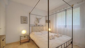 A four-poster bed with a skull decoration, a bedside table with a lamp, and a window with sheer curtains. - THE HORIZONS (Cannes)