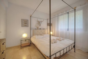 Ein Himmelbett mit Schädelverzierung, ein Nachttisch mit Lampe und ein Fenster mit transparenten Vorhängen.