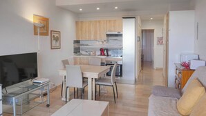 A modern living room with a flat-screen TV, a glass coffee table, a sofa, and a dining area with a table and chairs. - THE HORIZONS (Cannes)
