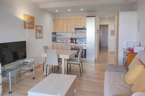 Ein modernes Wohnzimmer mit Flachbildfernseher, Glastisch, Sofa und Essbereich mit Tisch und Stühlen.