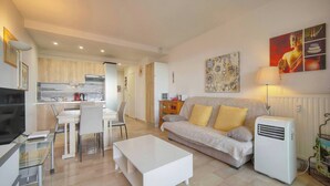 A modern living room with a sofa, coffee table, and a TV. There is a kitchen area with cabinets and a microwave. - THE HORIZONS (Cannes)