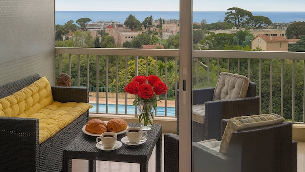 A balcony with wicker furniture, a table with croissants and coffee, and a vase of red roses. - THE HORIZONS (Cannes)