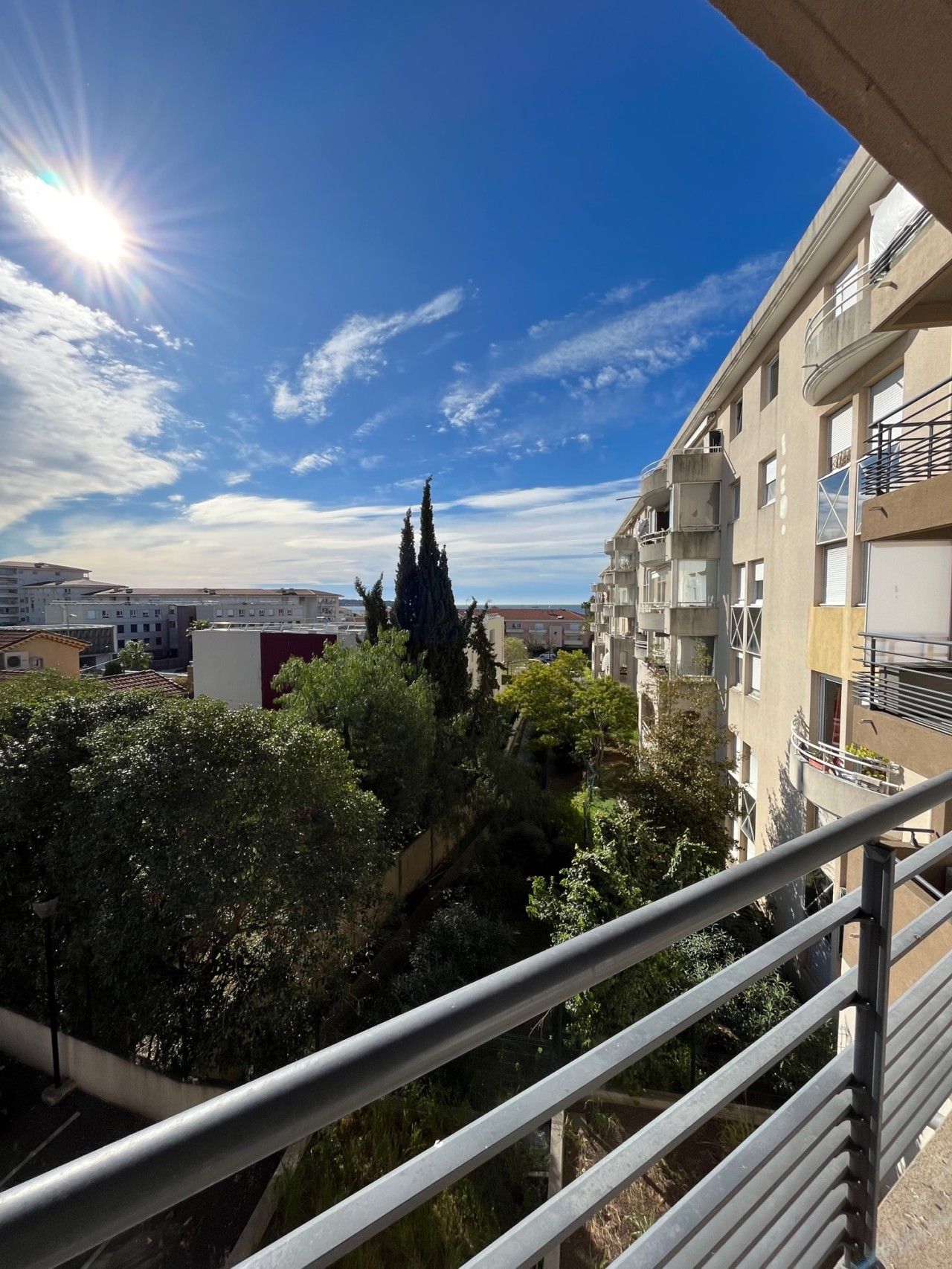 A balcony with a view of a residential area, including buildings and trees.
