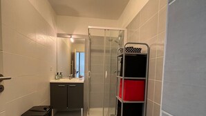 Un baño pequeño con inodoro, cabina de ducha, lavamanos y estante.
