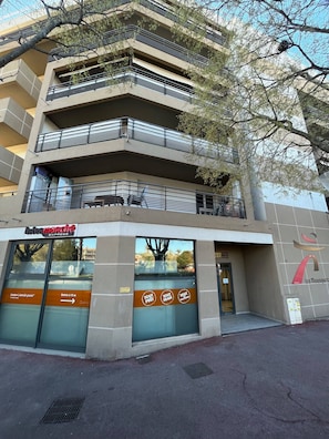 Un edificio a più piani con balconi, un negozio con insegna 'Intermarché Express' e un cartello che indica 'Ingresso a 15 metri'.