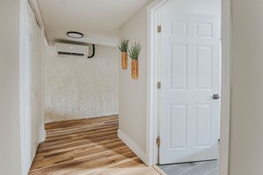 Un pasillo con suelo de madera, una puerta blanca y un equipo de aire acondicionado en la pared.