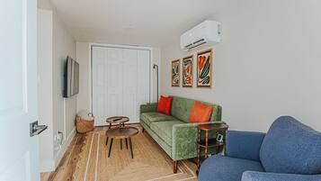 A living room with a green sofa, a blue sofa, a small table, a TV, and a door.