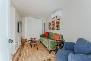 Una sala de estar con un sofá verde, un sofá azul, una mesita, un televisor y una puerta.