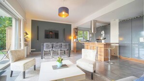 A modern living room with a white coffee table, two armchairs, a sofa, a dining area with a table and chairs, and a kitchen with a bar area. - FRGK Diane Elegance and Comfort in Antibes (Antibes)