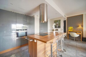 A modern kitchen with stainless steel appliances, a wooden island with bar stools, and a dining area with a table and chairs. - Frgk *Diane | Elegance and Comfort in Antibes* (Antibes)