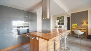 A modern kitchen with a central island, stainless steel appliances, and a dining area with a wooden table and bar stools. - FRGK Diane Elegance and Comfort in Antibes (Antibes)