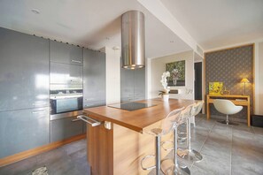 Eine moderne Küche mit einer zentralen Kochinsel, Edelstahlgeräten und einem Essbereich mit Holztisch und Barhocker.