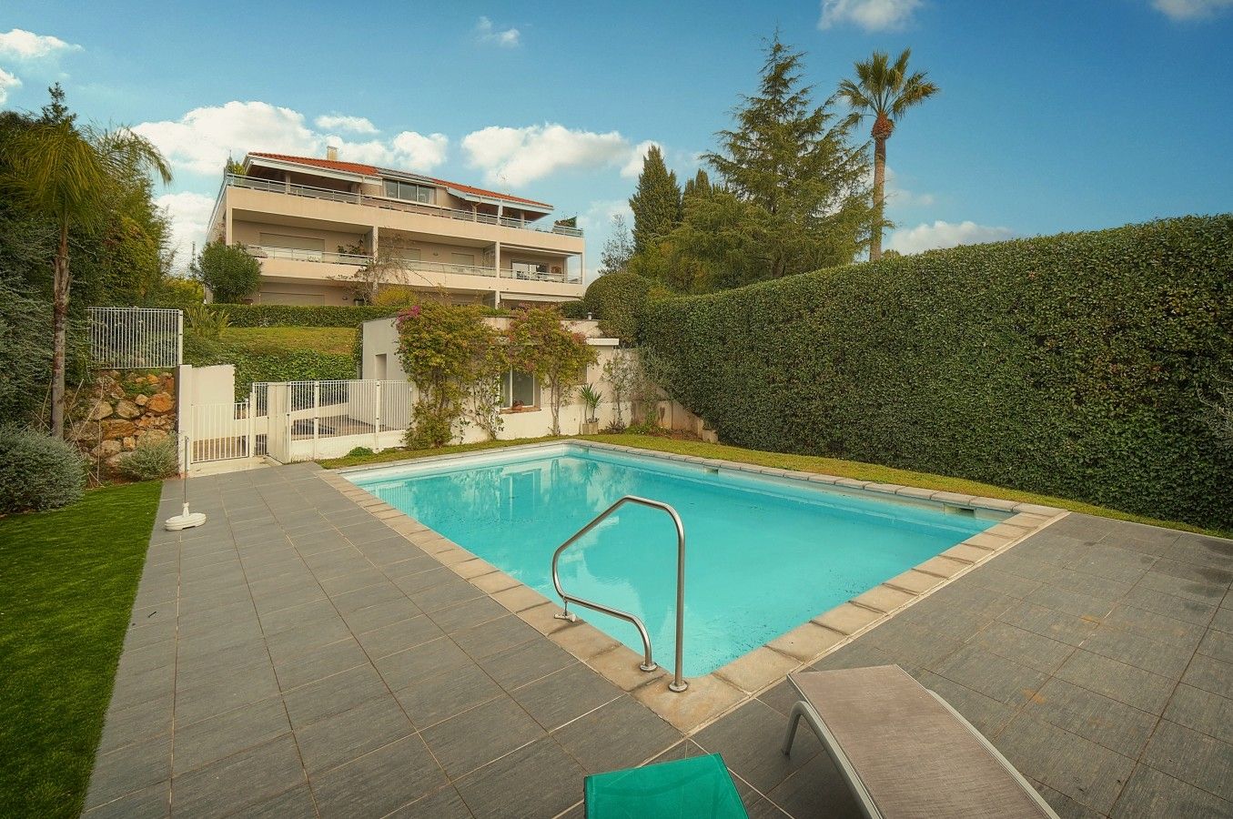 A rectangular swimming pool with a metal ladder, surrounded by a paved patio.