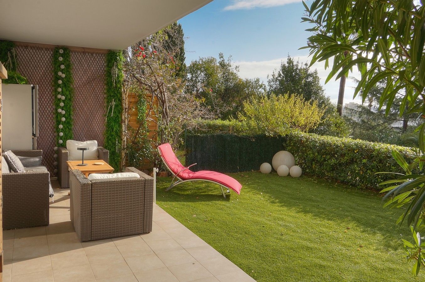 Un espace patio aménagé avec du mobilier d’extérieur, un fauteuil rouge et une pelouse bien entretenue.