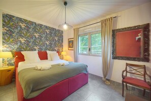 Una habitación de hotel con cama, ventana, silla, lámpara y pared con estampado floral.