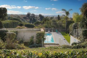 Ein Swimmingpool, umgeben von üppiger Vegetation und wolkenlosem Himmel.