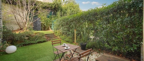 A patio with a wooden table and chairs, surrounded by a well-maintained garden with a variety of plants and a small lawn.