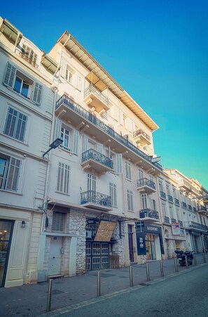 Un immeuble à plusieurs étages, doté de balcons, d’une devanture de magasin et surplombant un ciel dégagé.