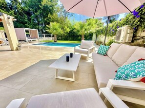 Ein Poolbereich mit einer weißen Couch, zwei weißen Stühlen, einem Tisch und einem Sonnenschirm.