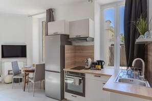 A compact kitchen with a refrigerator, oven, and a small dining area with a table and chairs. - Frgk Suquet Olivier 1-Bedroom Apartment with Charm and UltraFast WiFi (Cannes)