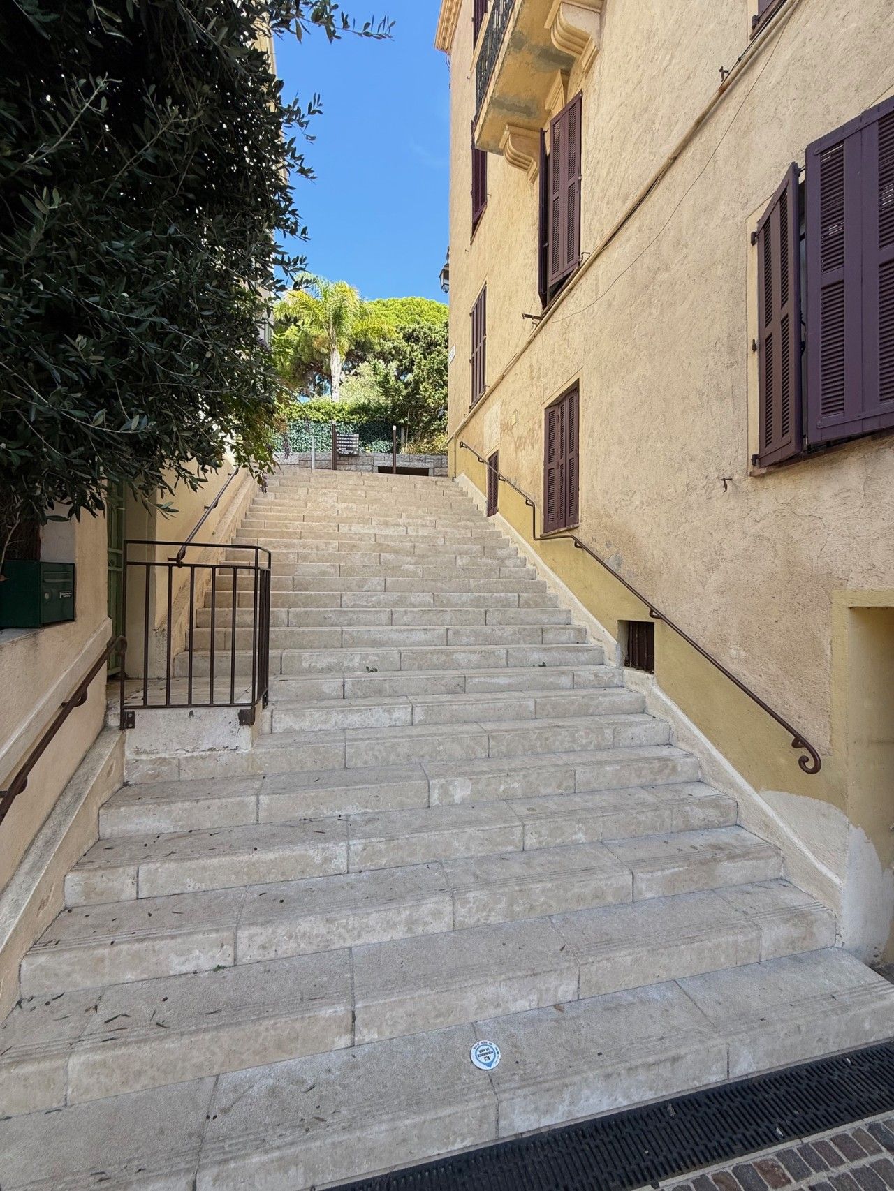 A stone staircase leading up to a building with a beige facade and dark shutters.