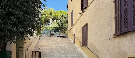A stone staircase leading up to a building with a beige facade and dark shutters.