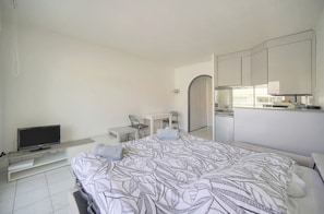 A bedroom with a bed, a desk, a chair, a television, and a kitchenette. - Frgk - Gallieni: A Quiet Studio (Cannes)