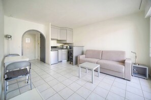 Ein modernes Wohnzimmer mit einer Couch, einem Couchtisch, einem Esstisch mit Stühlen, einer Küchenzeile und einem kleinen Beistelltisch.