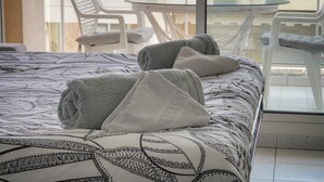 Sängyssä on kuviollinen vuodevaatesetti, kaksi rullalle taitettua pyyhettä ja parvekkeella on tuoleja ja pöytä.