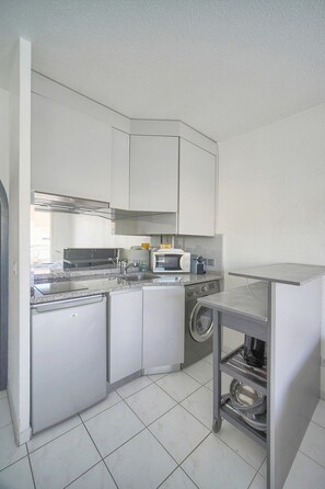 A compact kitchen with white cabinets, a built-in microwave, a washing machine, and a small countertop. - Frgk - Gallieni: A Quiet Studio (Cannes)