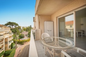 A balcony with a glass table and chairs, a sliding glass door, and a view of the surrounding buildings and greenery. - Frgk - Gallieni: A Quiet Studio (Cannes)