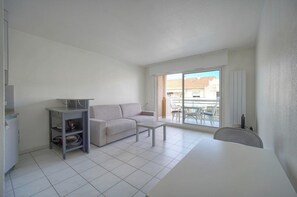 A modern living room with a sofa, a coffee table, and a small kitchen area with a cabinet. - Frgk - Gallieni: A Quiet Studio (Cannes)