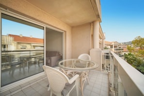 A balcony with a glass table and chairs, a sofa, and a sliding glass door leading to an outdoor area. - Frgk - Gallieni: A Quiet Studio (Cannes)