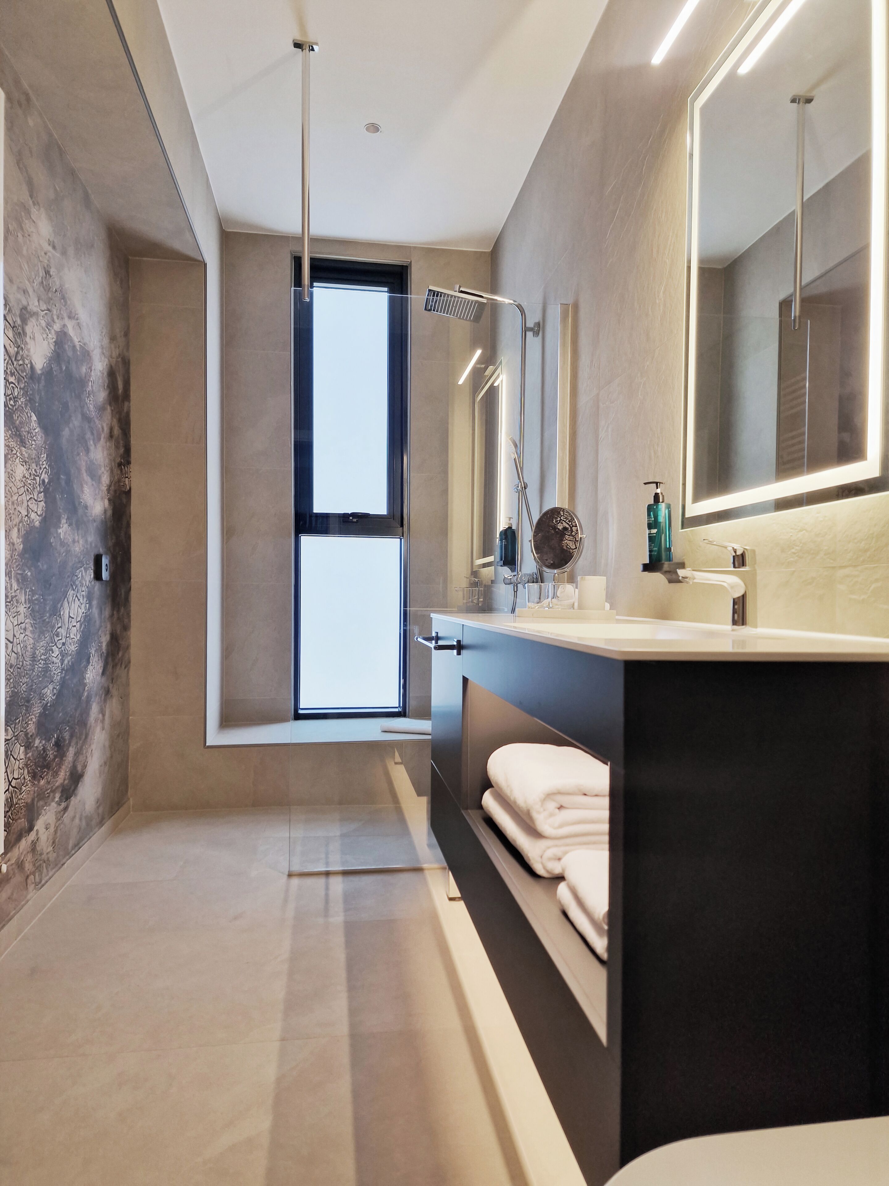 A modern bathroom with a large mirror, a shower, and a window.