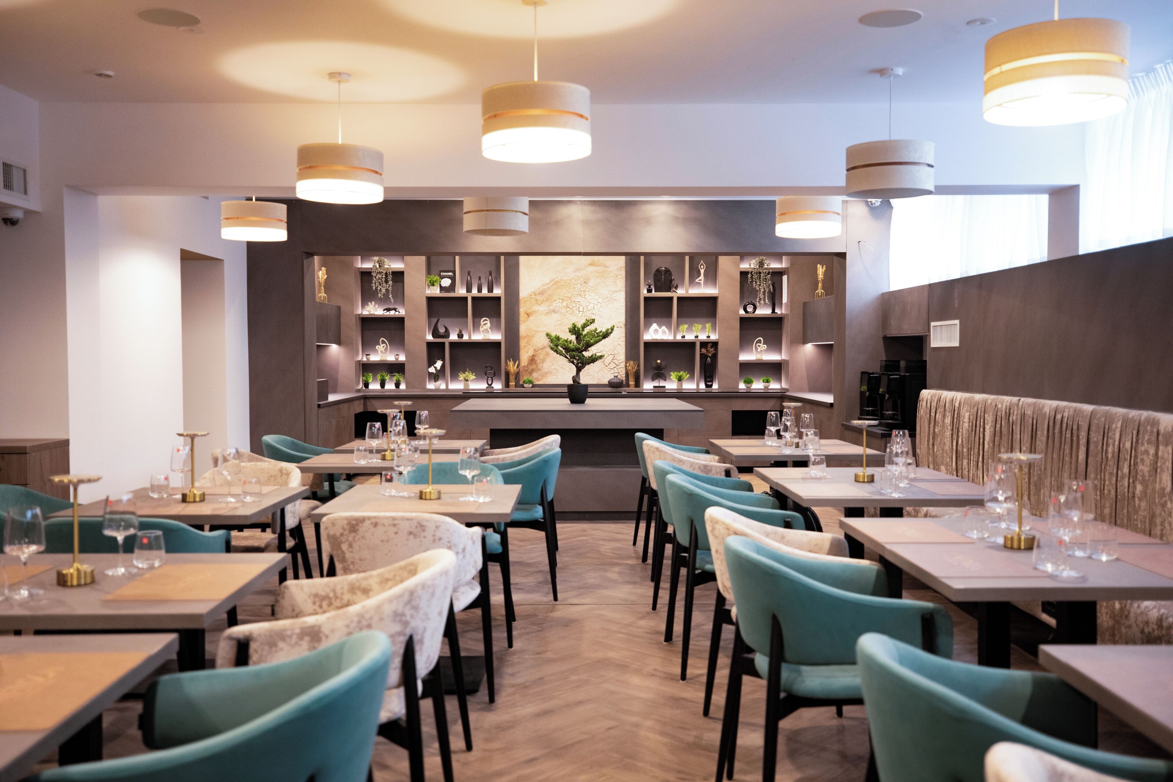 A restaurant interior with multiple tables and chairs, a bar area with shelves, and hanging pendant lights.