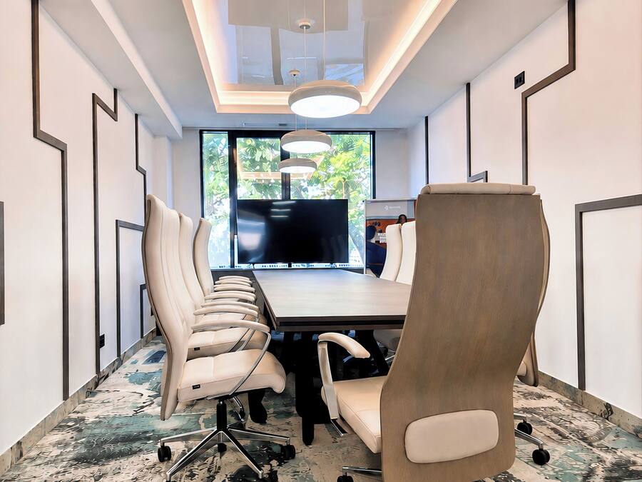 A conference room with a long table, multiple chairs, a large screen, and a patterned carpet.