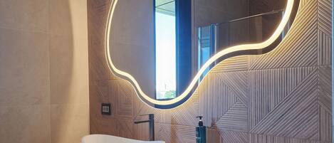 Un baño moderno con un espejo ovalado grande, un lavabo blanco tipo recipiente y un perchero para toallas.