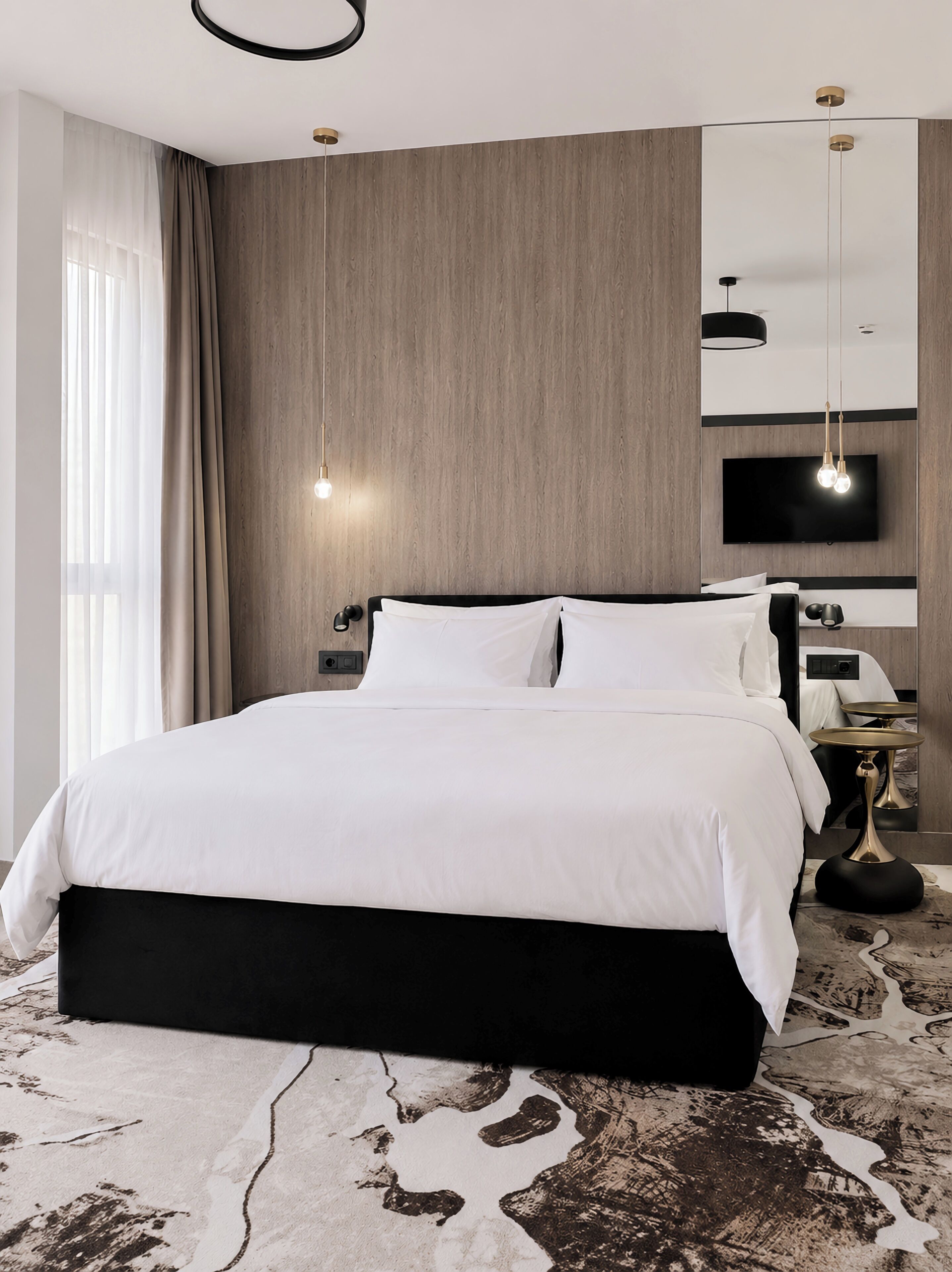 A modern hotel room with a large bed, a flat-screen TV, and a unique patterned rug.
