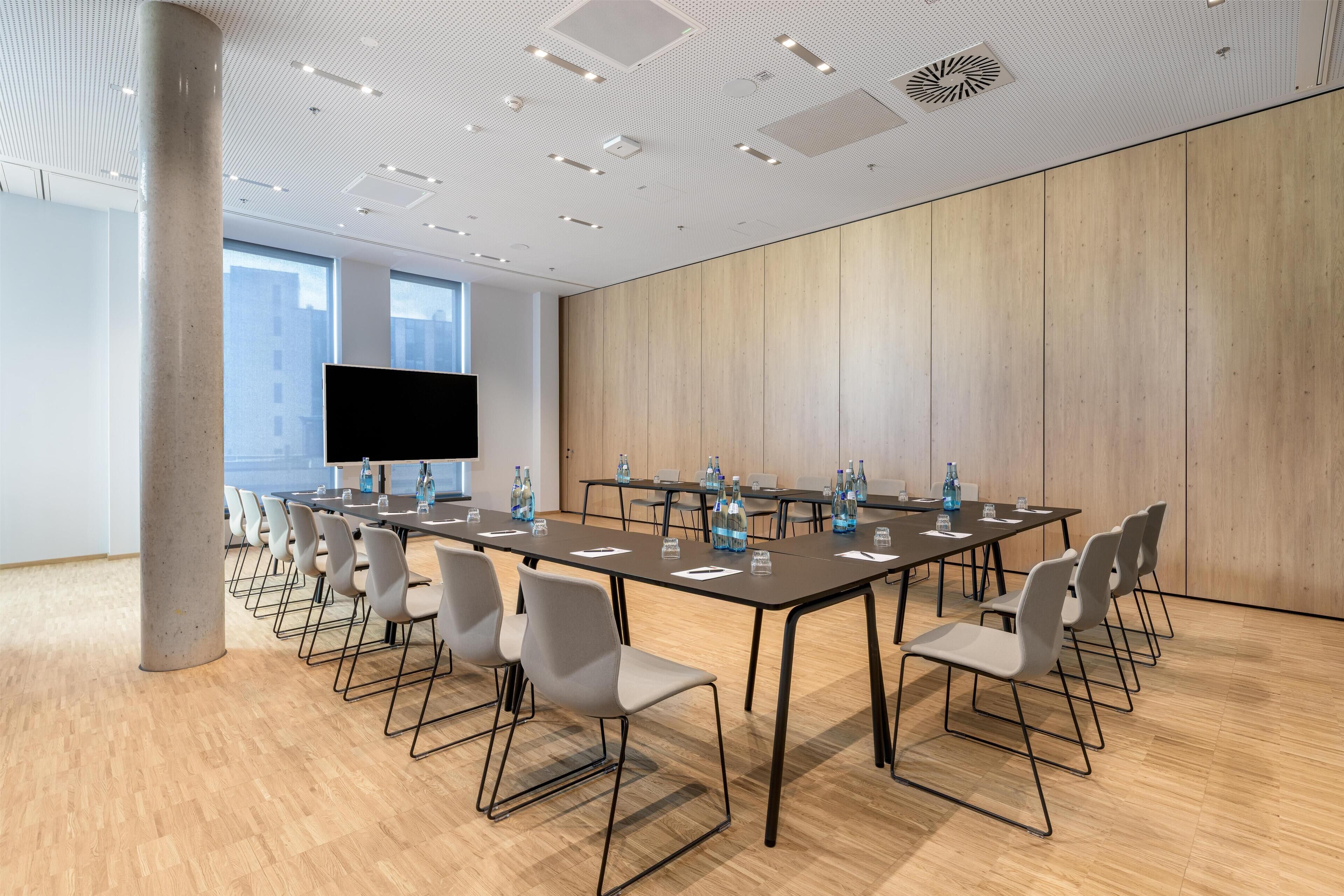 Un salón de conferencias con una larga mesa, sillas, un televisor de pantalla plana y vista a la ciudad.