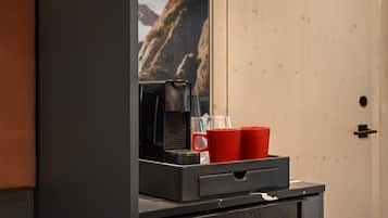 Une machine à café, deux tasses rouges et un verre sont posés sur un comptoir, avec une vue sur les montagnes en arrière-plan.
