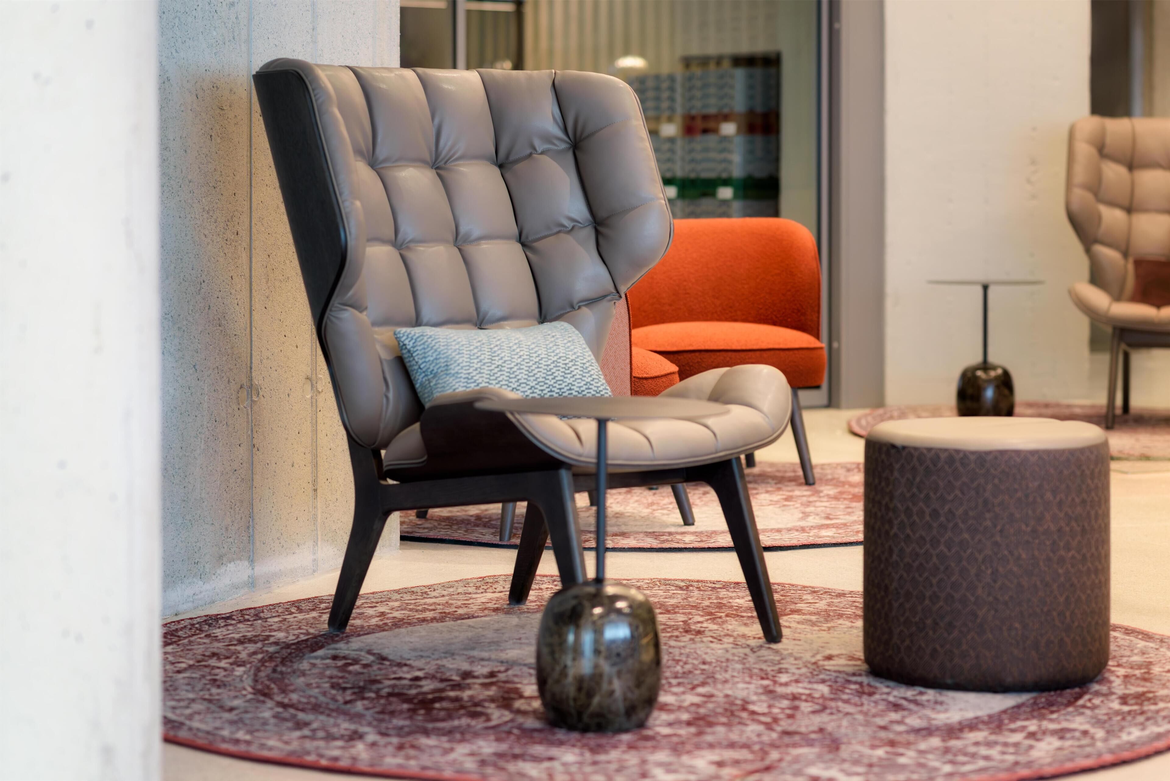 Un espacio lounge moderno con un sillón capitonado, un reposapiés redondo y una alfombra estampada.