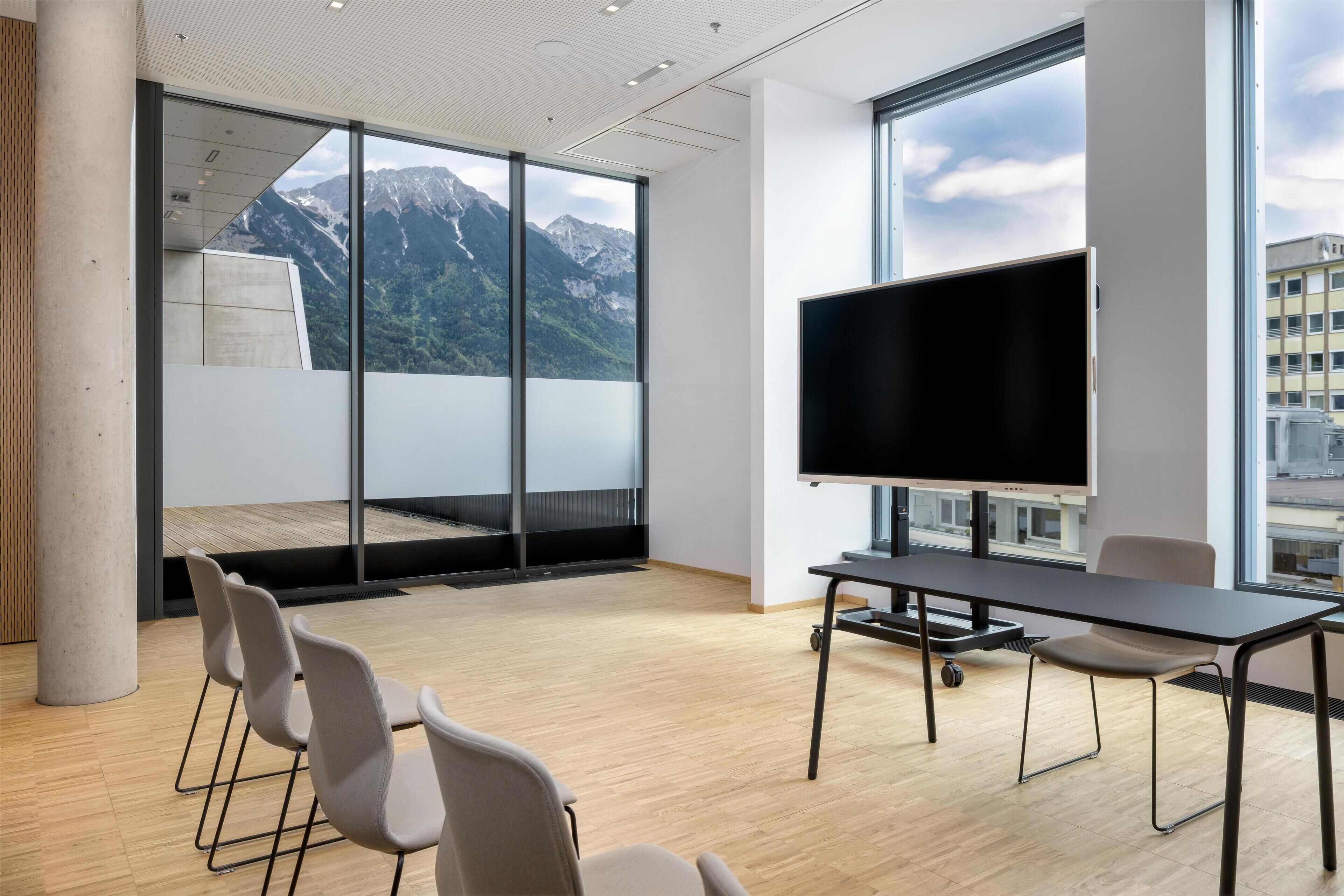A conference room with a large window, a flat-screen TV, and a wooden floor.