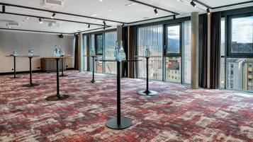 A hotel room with large windows, a red patterned carpet, and tables with water bottles.
