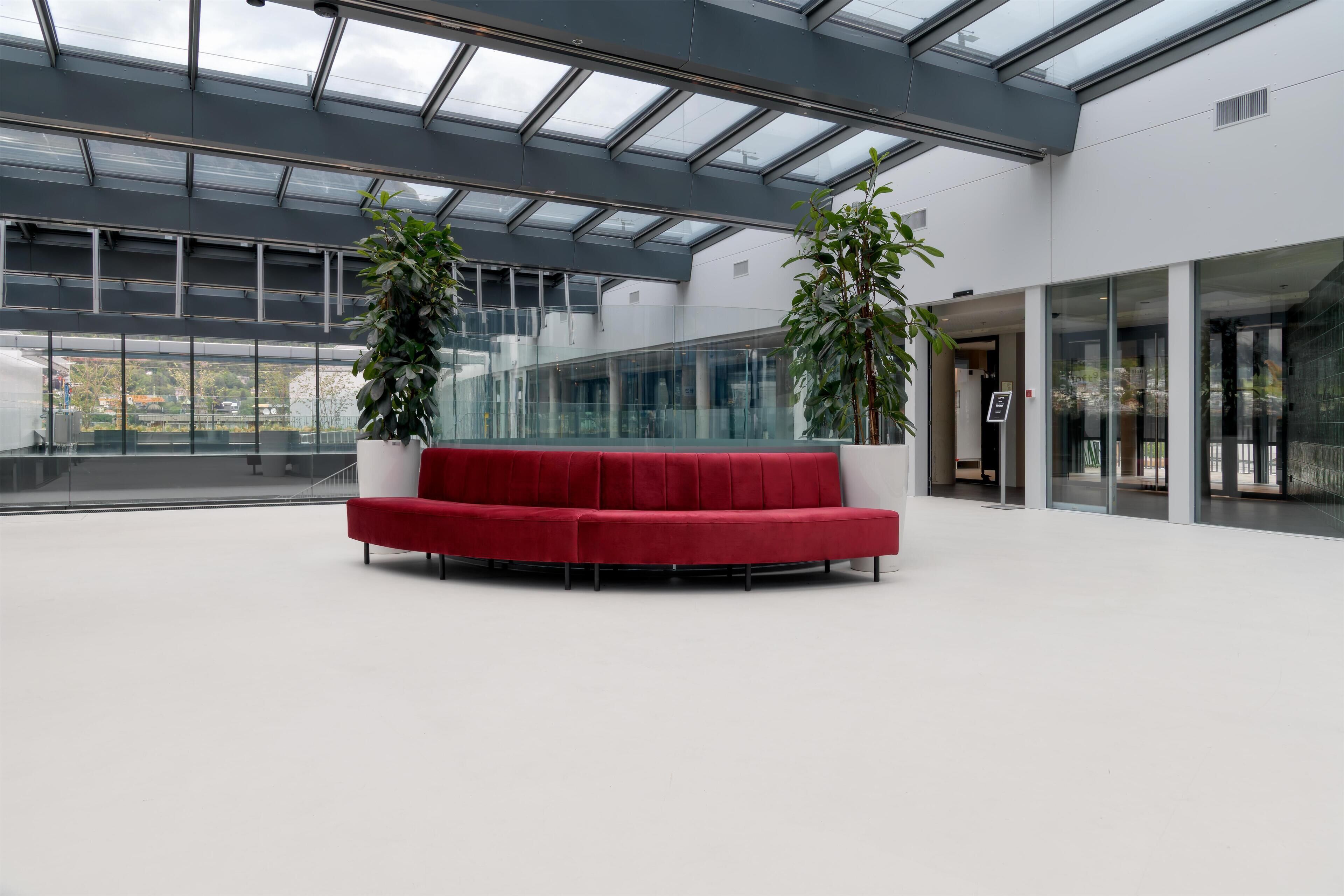 Un vestíbulo moderno con un sofá rojo, paredes de vidrio y plantas en macetas.
