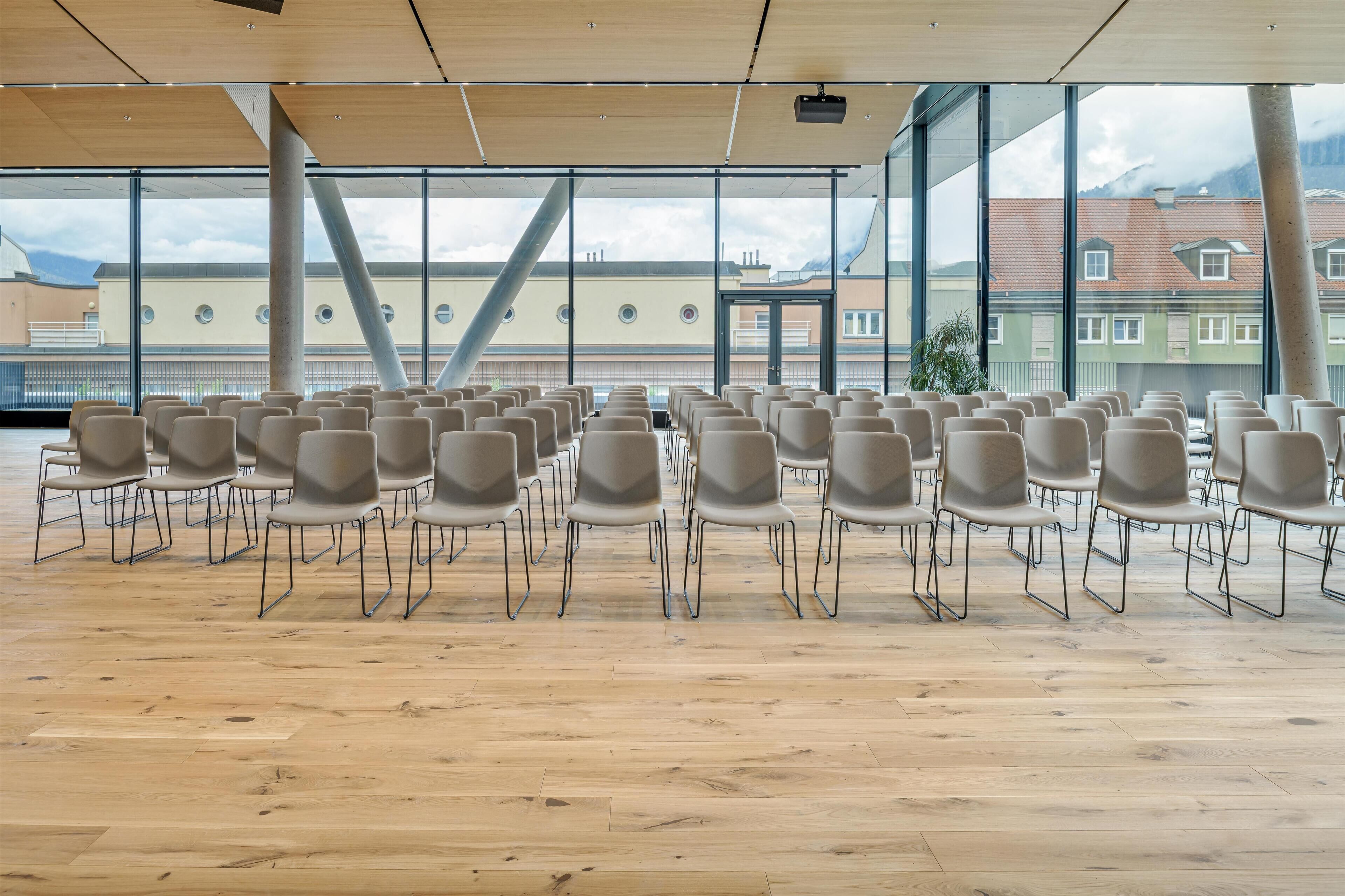 A conference room with rows of chairs, large windows, and a wooden floor.
